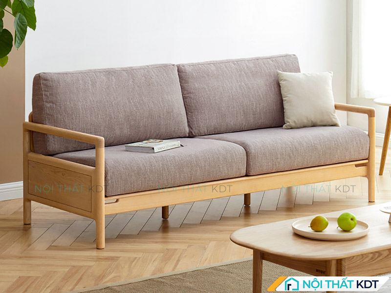 Chiếc sofa văng đôi được bố trí sát góc tường gần cửa sổ, đón ánh sáng tự nhiên dịu nhẹ, kết hợp hài hòa với bàn trà phía trước để tạo nên không gian tiếp khách gọn gàng, ấm cúng