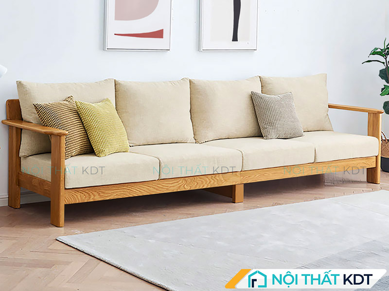 Chiếc sofa văng gỗ 4 chỗ được đặt sát tường trong phòng khách, kết hợp cùng thảm sàn sáng màu và cây xanh trang trí, tạo nên không gian ấm cúng và hiện đại