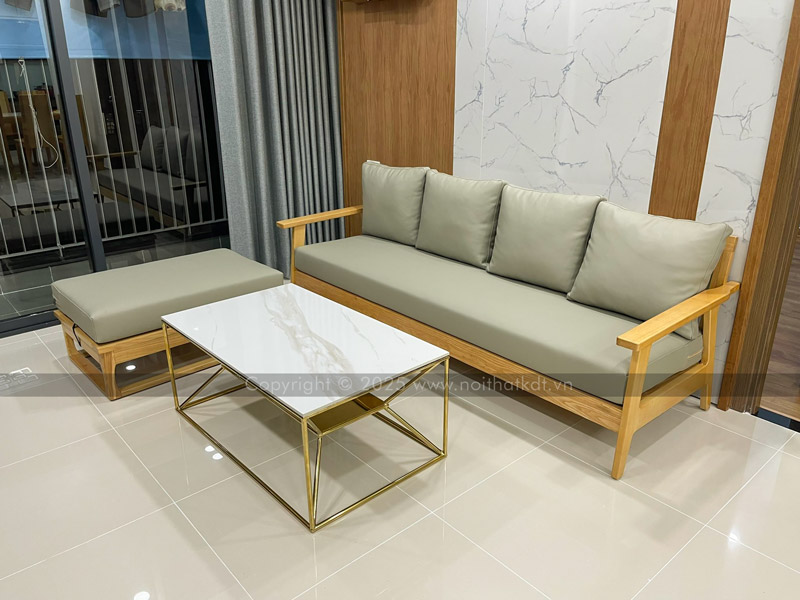 Sofa văng gỗ 3 chỗ được kê sát tường và gần cửa kính để đón ánh nắng tự nhiên, kết hợp với ghế đôn đặt ở góc trái tạo thành hình chữ L và bàn trà ở chính giữa nhằm tạo nên không gian tiếp khách hiện đại và tối giản
